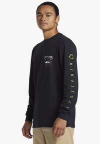 Čierna košeľa s dlhým rukávom s prednou grafikou planéty a hviezd, a s textom "Quiksilver" v zelenej farbe pozdĺž pravého rukávu.