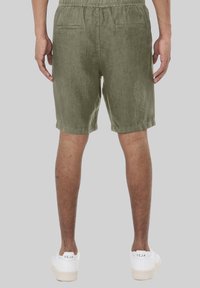 Olivgrüne Shorts mit lockerer Passform, ausgestattet mit einem elastischen Bund, Gesäßtaschen und einem strukturierten Stoff. Getragen mit weißen Sneakern.