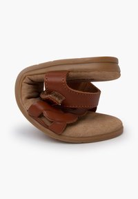 Sandalo marrone in pelle con design slip-on e interno morbido, caratterizzato da una larga fascia, dettagli testurizzati e suola in gomma flessibile.