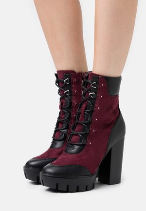 Bottines à talons bordeaux et noires en daim et cuir, avec un design à lacets, des éléments métalliques et des semelles texturées.