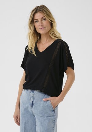 Top corto nero con scollo a V e maniche corte, caratterizzato da dettagli in pizzo geometrico lungo le spalle e i lati, abbinato a jeans azzurri dalla vestibilità rilassata.
