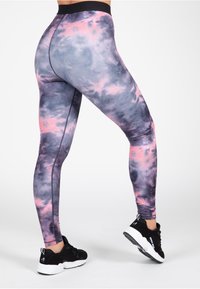 Hoge taille legging in een grijs en roze tie-dye patroon, met een gladde textuur en platte naden voor extra comfort. Gecombineerd met zwarte sneakers.