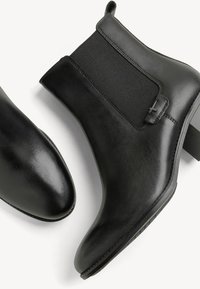 Botas de piel negras hasta el tobillo con paneles laterales elásticos, punteras redondeadas, tacón bajo en bloque y detalles de costura sutiles. Textura suave en toda su superficie.