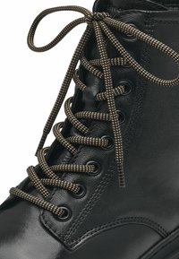 Botte en cuir noir avec bout rond, dessus texturé et lacets marron foncé mouchetés. Présente des œillets en métal et des coutures renforcées le long des coutures.