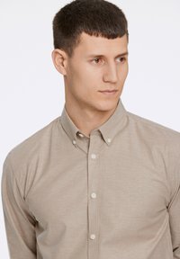 Camicia button-up beige chiaro con colletto e piccoli bottoni, realizzata in tessuto liscio, presenta una vestibilità slim e una lieve texture.