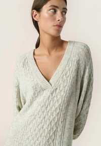 Maglione grigio chiaro lavorato a maglia con scollo a V profondo, caratterizzato da un motivo a trecce e maniche strutturate. Materiale morbido, vestibilità comoda.