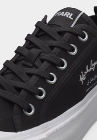 Μαύρο χαμηλό αθλητικό παπούτσι με μαύρα κορδόνια, ασημένιες τρύπες για τα κορδόνια, λευκή σόλα και λευκή κεντημένη επωνυμία Karl Lagerfeld στο πλάι και στη γλώσσα.