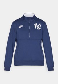 Námornícky sveter s štvrtinovým zipsom, s bielym logom Nike a emblémom New York Yankees. Vyrobený z mäkkej látky s dlhými rukávmi.