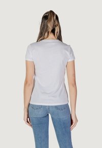 Weißes Kurzarmshirt mit Rundhalsausschnitt, glattem Baumwollstoff und taillierter Passform. Kombiniert mit hellblauen Jeans.