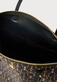 Bolsa estampada em preto e castanho com fecho dourado, aberta para mostrar um interior vazio e forro de tecido com um bolso interior.