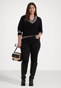 Μαύρο πλεκτό πουλόβερ με V-λαιμόκοψη και λευκές ρίγες, σε συνδυασμό με μαύρα τζιν και μαύρες δερμάτινες μπότες μέχρι το γόνατο, κρατώντας μια τσάντα δύο τόνων.