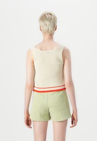 Heklet tank topp i off-white med ribbet tekstur, har en rød og hvit stripete kant. Parret med grønne kordfløyelsshorts, som viser bakvinkel.