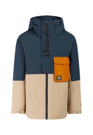 Jongen met een colorblock navy en beige winterjas en broek, oranje muts en zwarte laarzen, staand met handen in de zakken.