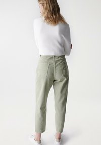 Světle zelené kalhoty s vysokým pasem a zúženými nohavicemi, se dvěma zadními kapsami a hladkým bavlněným povrchem, spárované s bílým pleteným svetr.