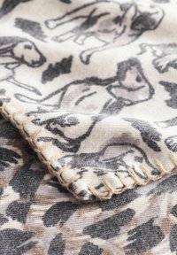 Couverture en tissu avec un motif de chiens noirs et gris sur fond crème, avec un bord à franges et une finition texturée dans des tons beiges.