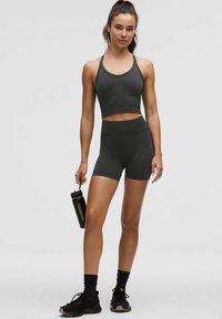 Tamsiai pilkas sportinis komplektas, sudarytas iš trumpaaukštės tankų ir aukšto liemens šortų, abu pagaminti iš glotnaus, elastingo audinio. Komplekte yra juodas vandens butelis.