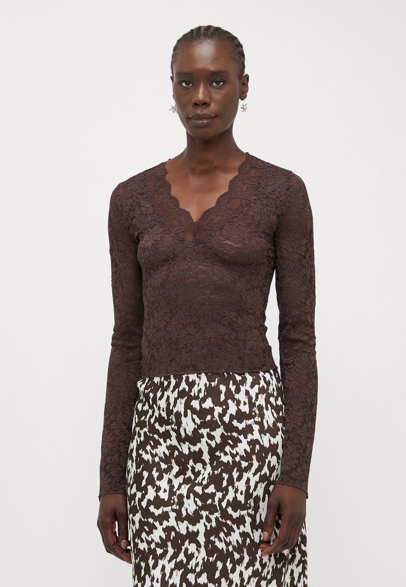 Brown lace long-sleeve top with a scalloped neckline, featuring intricate floral patterns. Paired with a patterned brown and white skirt.