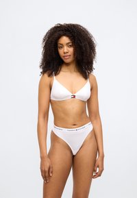 Balts trijstūra formas bralets ar plānām regulējamām lencēm un mazu logotipu. Atbilstošas baltas biksītes ar elastīgu jostasvietu, uz kuras redzams zīmola nosaukums.