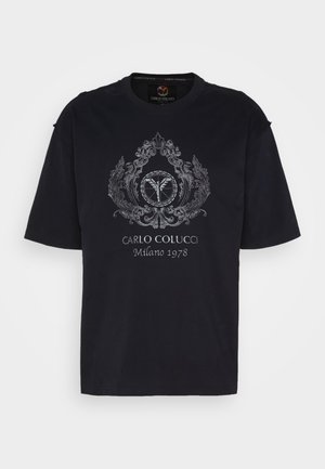 Black short-sleeve T-shirt with ornate silver emblem, including wings and leaves, and text "CARLO COLUCCI Milano 1978" on front.