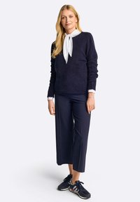 Maglione in maglia blu scuro con vestibilità comoda, camicia bianca sotto e pantaloni a gamba larga blu abbinati; completato con scarpe sportive nere.