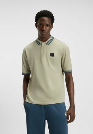Kortærmet polo i lys olivengrøn med en marineblå stribet krave, tre knapper og et lille sort logo patch på brystet.