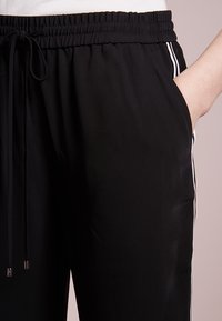 Svarta sportbyxor med resårmidja, justerbar dragsko, sidofickor och vita sidostreck. Slät tygkvalitet.