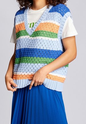 Personne portant un gilet tricoté multicolore avec des rayures bleues, vertes, orange et blanches sur un t-shirt blanc et une jupe plissée bleue.