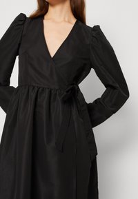 Svart omlottklänning med långa ärmar, djup V-ringning och resår i midjan. Tillverkad av mjukt tyg, med en detalj i form av en knytning i sidan.
