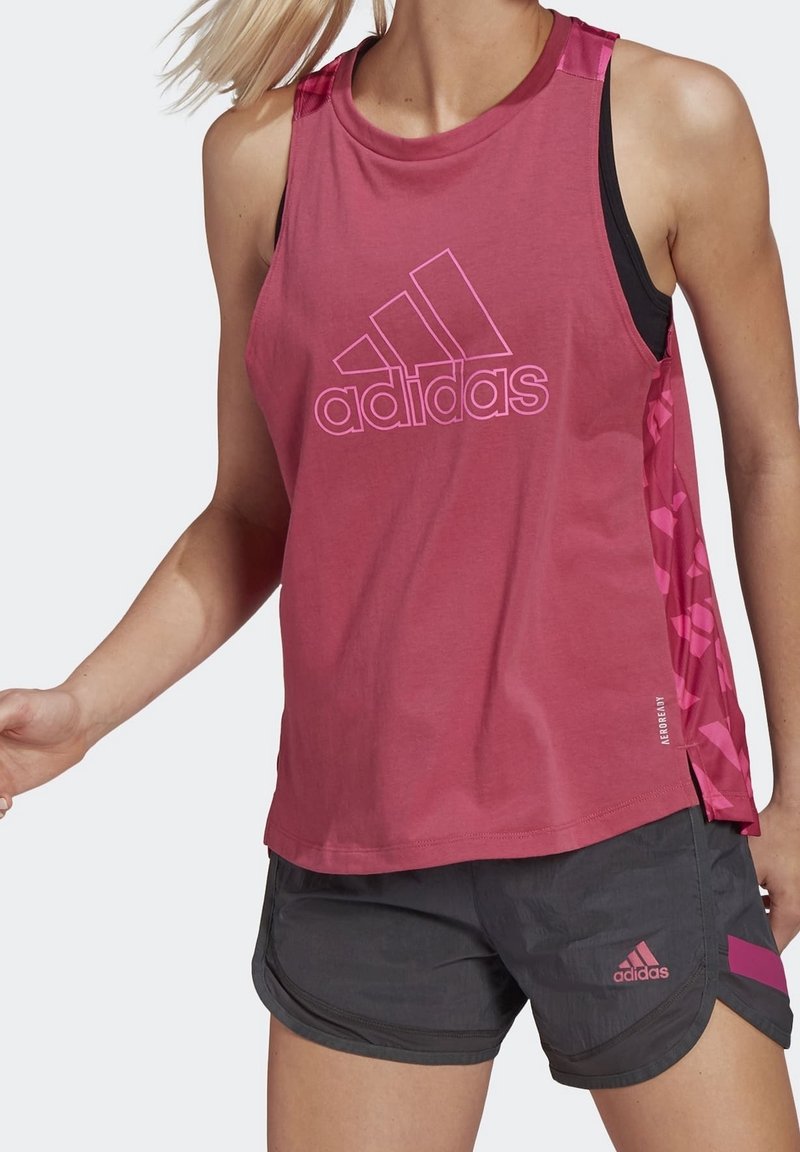 Różowy, bezrękawnik sportowy z dużym białym logo "adidas", w połączeniu z ciemnoszarymi szortami z różowymi akcentami i lekką, teksturowaną tkaniną.