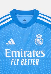 Maglia azzurra chiara con colletto rotondo, caratterizzata da strisce bianche Adidas sulle maniche e logo "Emirates FLY BETTER" in testo bianco.
