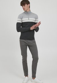 Grå zip-up genser med hvite og lysegrå horisontale striper, satt sammen med slanke mørk grå bukser og hvite sneakers. Glatt tekstur.
