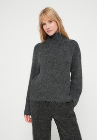 Pullover de gola alta cinza escuro com uma textura macia e felpuda, apresentando ombros deslocados e um corte descontraído. Abertura desfiada na barra inferior.