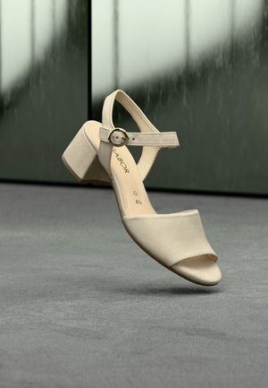 Beige sandaal met hoge hak en open neus, voorzien van een brede band en een gespsluiting op de enkelband. Gladde textuur en een stevige hiel.