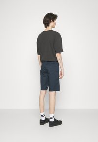 T-shirt gris oversized avec des manches retroussées, associé à un short navy. Les détails comprennent un petit logo sur le short et des chaussettes blanches rayées.
