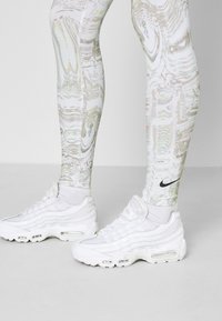 Vita mönstrade leggings med iriserande designer, tillsammans med vita sneakers med transparenta paneler och synlig luftdämpning.