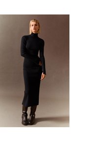 Černé úpletem pletené šaty s vysokým límcem, dlouh�ými rukávy, přiléhavým střihem a midi délkou, doplněné o tmavě hnědé boty na podpatku s přezkami.
