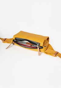 Geel schoudertas met een ritsvak, voorzien van leren accenten en een textuurstof interieur in grijs en rood met een ruitpatroon.