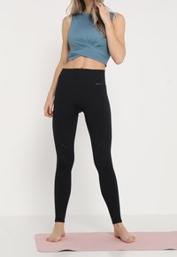 Czarne legginsy z wysokim stanem z wycięciami i gładką fakturą. Tealowy krótki top z twisted front w miękkim materiale.