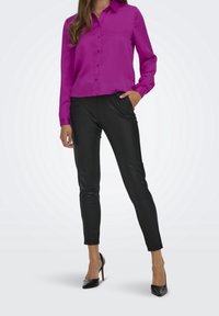 Camisa de botones magenta de manga larga combinada con pantalones ajustados de faux cuero negros y tacones de aguja negros, creando una silueta elegante.
