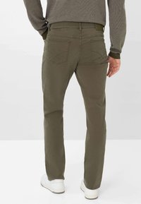 Pantaloni dritti color verde oliva in misto cotone, con tasche posteriori e dettagli di cucitura sottili, abbinati a scarpe bianche.