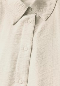 Lichtgekleurde, gestructureerde stoffen shirt met een puntig col en zes knoopsluitingen, met een licht kreukelige uitstraling.