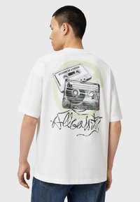 Tricou alb din bumbac cu un imprimeu grafic cu două casete audio și textul "Mesaj pentru un Viitor" pe partea din spate. Croială lejeră.