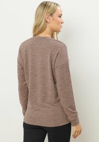 Brązowy, teksturowany sweter dziany z okrągłym dekoltem i luźnym krojem. Długie rękawy z prążkowanym mankietem i lekko zaokrąglonym dołem.