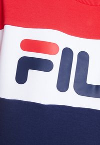 Tissu rouge, blanc et bleu marine avec un logo audacieux présentant des lettres en bloc stylisées bleu marine et rouge sur la section blanche.