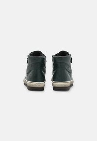 Green leather ankle boots with rounded design, textured soles, and contrasting white rubber accents. Side zippers and soft lining visible.