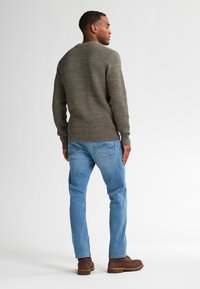 Olijfgroene gebreide trui met textuurpatroon, gecombineerd met lichtblauwe jeans en bruine enkellaarsjes, bekeken vanaf de achterkant.
