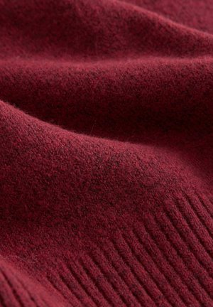Burgundy ulltyg med en mjuk textur, med ett ribbat mönster vid kanten. Materialet verkar varmt och tätt.