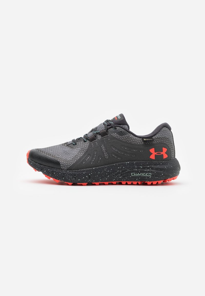 Chaussure de course Under Armour noire et grise avec semelle extérieure rouge et logo, semelle intermédiaire texturée et fermeture à lacets sur fond blanc.