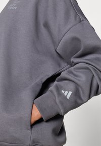 Pilkas džemperis su laisvu kirpimu, ribinėmis rankogaliais, šonine kišene ir mažu atspindinčiu logotipu ant rankovės. Minkšta, tekstūruota medvilnės mišinys.