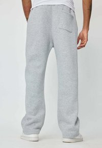 Un pantalon de jogging gris clair avec une coupe décontractée, doté d'une poche arrière et de poignets côtelés, fabriqué en coton doux et texturé.